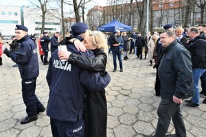 zdjęcie przedstawia policjanta ściskanego przez matkę, obok inni uczestnicy uroczystości