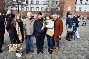 zdjęcie przedstawia nową policjantkę z kwiatami i rodziną pozującą do pamiątkowego zdjęcia