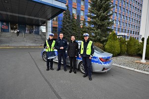zdjęcie przedstawia policjantów ruchu drogowego pozujących z wygranym aukcję na tle radiowozu i komendy