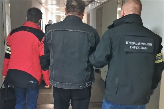 Zdjęcie. Widoczni dwaj policjanci z opaskami z napisem POLICJA prowadzący osobę zatrzymaną