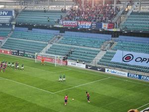 Zdjęcie. Widoczny fragment stadionu, piłkarze i kibice