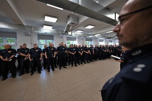 Zdjęcie. Widoczna sala, na której w szeregu stoi grupa kilkudziesięciu umundurowanych policjantów