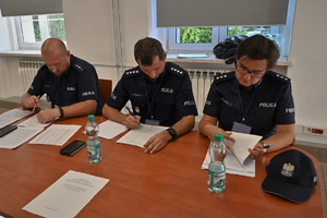 Zdjęcie. Widoczni siedzący przy stole umundurowani policjanci na sali