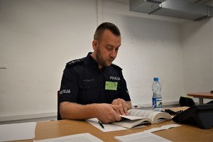 Zdjęcie. Widoczni siedzący przy stole umundurowani policjanci na sali