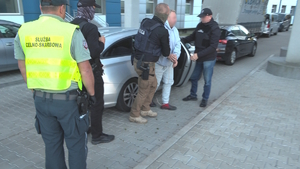 Policjanci i funkcjonariusze służby celno-skarbowej w kamizelkach wyprowadzą zatrzymanego mężczyznę w kajdankach z samochodu