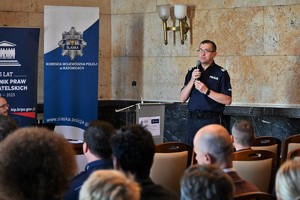 Zdjęcie. Komendant Wojewódzki Policji z mikrofonem w sali marmurowej