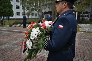 Zdjęcie. Umundurowany policjant trzymający wieniec kwiatów na terenie przed Grobem Policjanta Polskiego