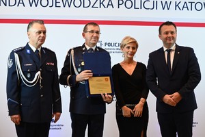 Zdjęcie przedstawia policjanta, policjanta trzymającego dyplom, kobietę i mężczyznę
