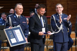 Zdjęcie przedstawia policjanta trzymającego dyplom, mężczyznę oraz policjanta bijącego brawo