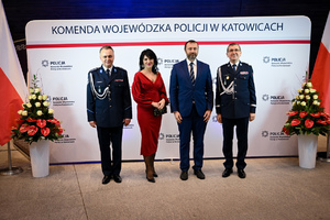Zdjęcie przedstawia dwóch policjantów, kobietę i mężczyznę, osoby stoją przed napisem Komenda Wojewódzka Policji w Katowicach
