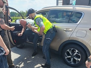 Zdjęcie funkcjonariusza w trackie obezwładniania osoby wyprowadzanej z pojazdu.