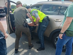 Zdjęcie osoby zatrzymanej prowadzonej w kajdankach przez funkcjonariuszy KAS.