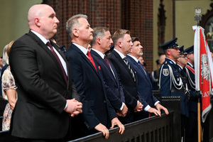 kolorowe zdjęcie przedstawiające mężczyzn w garniturach oraz policjantów kompani honorowej