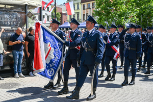 kolorowe zdjęcie policjantów kompani honorowej maszerujących ulicami miasta z sztandarem