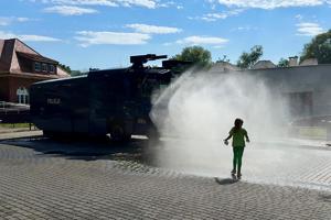 kolorowe zdjęcie przedstawiające pojazd Tajfun lejący wodą, w tle znajduje się dziecko