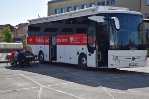 krwiobus czerwono - biały  na parkingu komendy, obok siedzą przy stolikach osoby chętne do odaania krwi