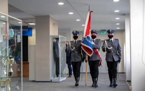 Poczet sztandarowy wchodzi na sala. Trzy osoby. Środkowy dzierży sztandar