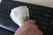 dłoń trzymająca polskie pieniądze nad klawiaturą komputera