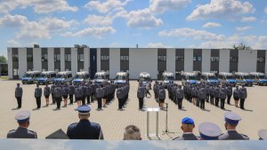 Widok na cały plac zza pleców kadry kierowniczej. Widok na radiowozy i policjantów na placu