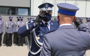 Policjant otrzymuje rozkaz mianowania od komendanta i salutuje. Widok zza pleców.