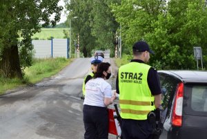 policjantka i pracownicy PKP wręczają kierowcy ulotkę, w tle przejazd kolejowy