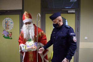 zastępca Komendanta Miejskiego Policji w Krakowie nadkomisarz Paweł Jastrząb pomagający Mikołajowi wręczać dzieciom prezenty.