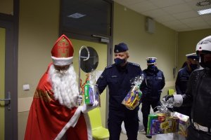 Zastępca Komendanta Miejskiego Policji w Krakowie nadkomisarz Paweł Jastrząb pomagający Mikołajowi wręczać dzieciom prezenty.