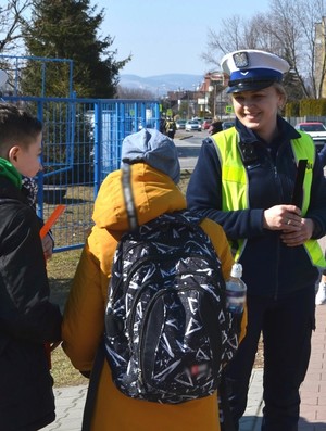 policjantka drogówki, obok uczniowie z odblaskowymi opaskami