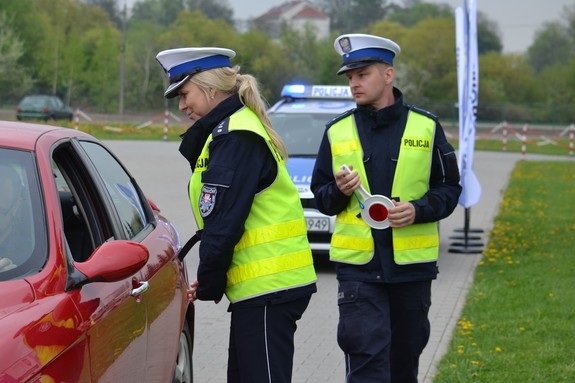 Policjantka ruchu drogowego podczas kontroli drogowej przedstawia kierującemu powód zatrzymania. Policjant ruchu drogowego asystuje.