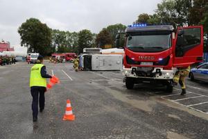 Policjant rozkłada stożek drogowy w tle wóz strażacki