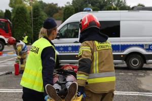 Policjantka ze strażakiem niosą ranną osobę na noszach