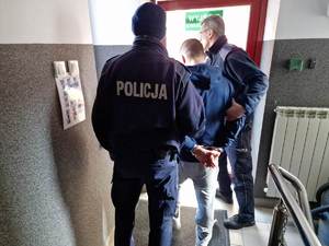 umundurowani policjanci otwierają drzwi do wyjścia z budynku zatrzymany skuty