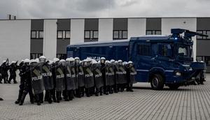 Policjanci Nieetatowych Pododdziałów Prewencji Idący w szyku. Obok nich jedzie armatka wodna