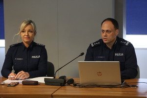 policjant i policjantka siedzą przy stoliku. policjant mówi do mikrofonu