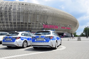 czterech umundurowanych policjantów patrolujących rejon Tauron Areny. Po lewej stronie widać dwa oznakowane radiowozy