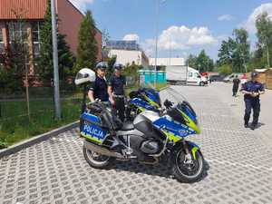 Dwaj polijanci rychu drogowego przy motocyklach. Na terenie obosktu sportowego, gdzie odbywaja się zawody sumo. W tle ovbiekt sporttowy, ulica i zaparkone auta.