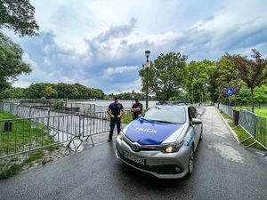 dwóch umundurowanych policjantów stojących przy radiowozie. W tle widać zalew na którym rozgrywane są zawody triathlonu