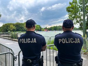 dwóch umundurowanych policjantów stojących tyłem do zdjęcia obserwuje zalew na którym rozgrywane są zawody triathlonu