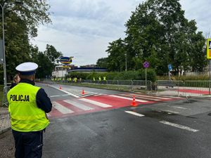 policjant ruchu drogowego srojący przy drodze obserwuje osoby w kamizelkach odblaskowych idące chodnikiem