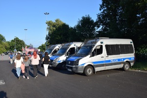 trzy oznakowane radiowozy stojące na parkingu w rejonie stadionu na ul. Reymonta. Przed pojazdami widać kilka idących osób