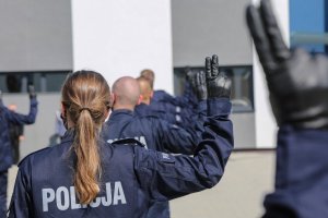 12. Policjanta z uniesionymi palcami podczas ślubowania, w tle dłonie innych ślubujących uniesione w górę