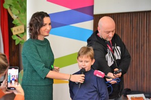 Członek Zarządu Województwa Małopolskiego - Pani Marta Malec-Lech  rozmawia przy użyciu mikrofonu z uczniem szkoły, obok dziennikarz Rmf Maxx nagrywający rozmowę mikrofonem