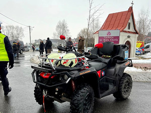 qud, obok idący policjant, w tle ludzie i zaparkowany radiowóz oraz kapliczka