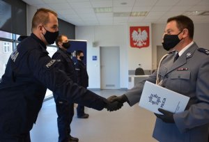 komendant z Oławy wręcza akt mianowania nowemu policjantowi, a tle widać pozostałych uczestników uroczystości