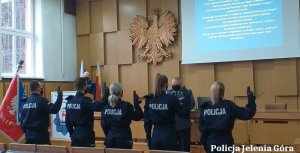 na sali policjanci z uniesioną prawą rękę wymawia rotę ślubowania, w tle widać pozostałych uczestników uroczystości