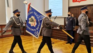 policjanci ze sztandarem wychodzą z sali, w tle widać innych policjantów