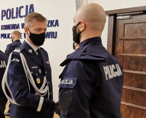 Komendant gratuluje nowym policjantom, wręcza im teczki z aktami mianowania, w tle widać innych policjantów