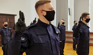 nowi policjanci trzymają uniesioną prawą rękę i wymawiają słowa roty ślubowania, w tle widać pozostałych policjantów biorących udział w uroczystości