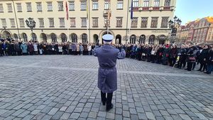 zgromadzeni ludzie na rynku wrocławskim wokół dyrygenta orkiestry policyjnej zwróconego przodem do chóru