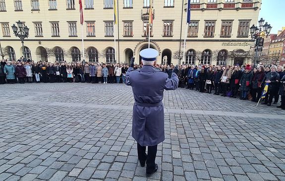 zgromadzeni ludzie na rynku wrocławskim wokół dyrygenta orkiestry policyjnej zwróconego przodem do chóru